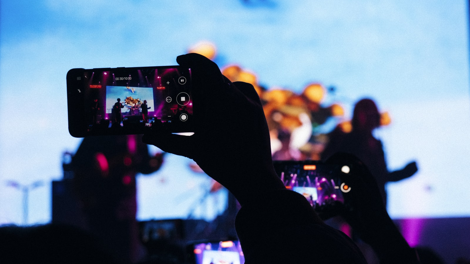 Hand holding a smartphone filming a concert